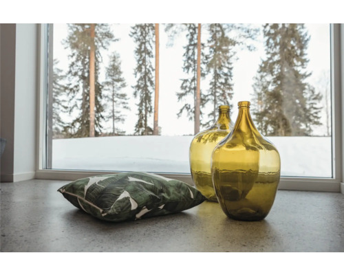 Dekorativa glasballonger och en kudde med bladtryck framför ett fönster med utsikt över ett vinterlandskap