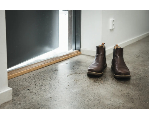 Ett par läderstövlar står framför en öppen dörr på ett betonggolv.