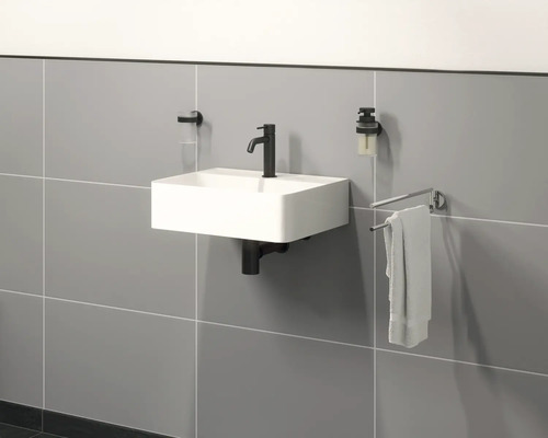 Hängande tvättställ med kran, tvåldispenser, tandborstmugg och handdukshållare på en vägg