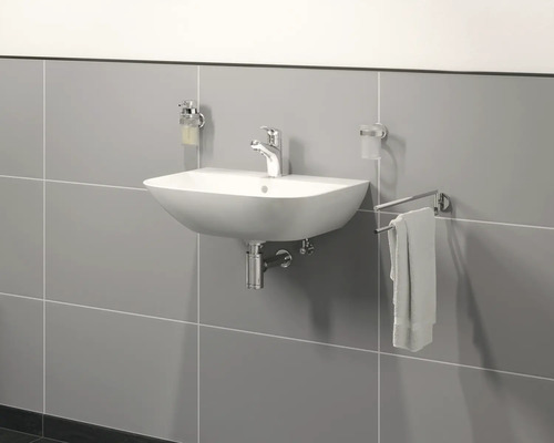 Keramisk tvättställ med armatur, tvålpump, tandborstmugghållare och handdukshållare på en grå vägg