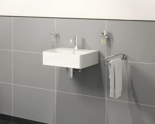 Vägghängd tvättställ med kran, tvålpump, handduk och tandborstmugghållare i ett badrum