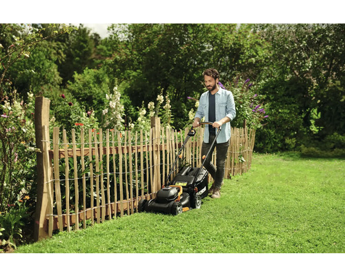 Man klipper gräs med en gräsklippare i en trädgård