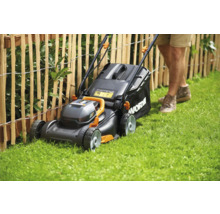 Gräsklippare i drift på gräsmatta framför trästaket