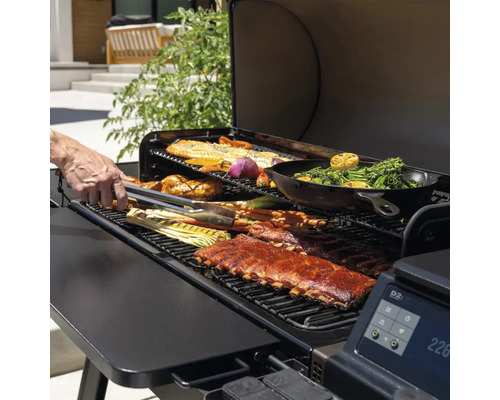 En grill med revbensspjäll, fisk och grönsaker som vänds med en tång.