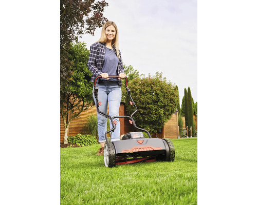 Kvinna använder cylinderklippare i trädgården.