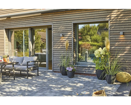 Terrass med stenläggning, trädgårdsmöbler, växter och träfasad