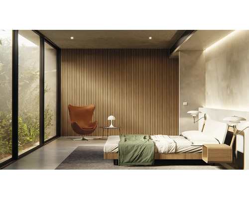 Ljust sovrum med säng, fåtölj, lampa och stort fönster med utsikt över grönområde.