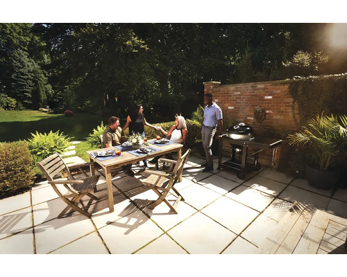 Grupp av människor sitter vid ett trädgårdsbord med en grill i bakgrunden