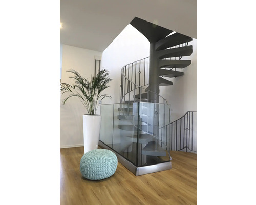 Interiörbild med spiraltrappa, glasräcke, växt och sittpuff