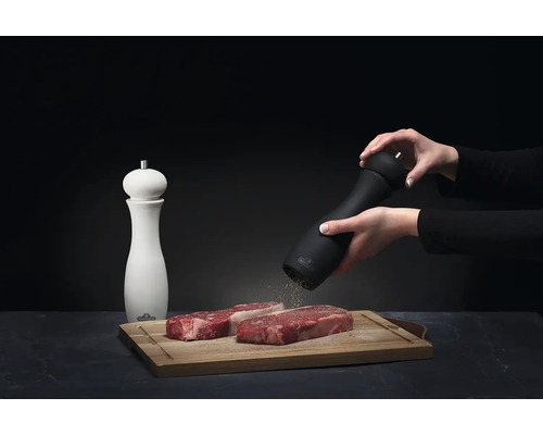 Pepparkvarn och biffar på skärbräda, en person kryddar köttet.