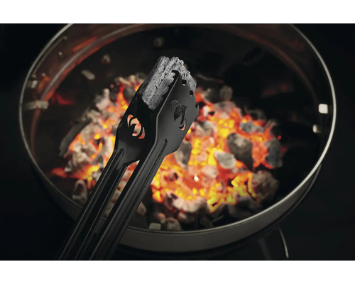 Grilltång håller grillkol över glödande kol i grillen