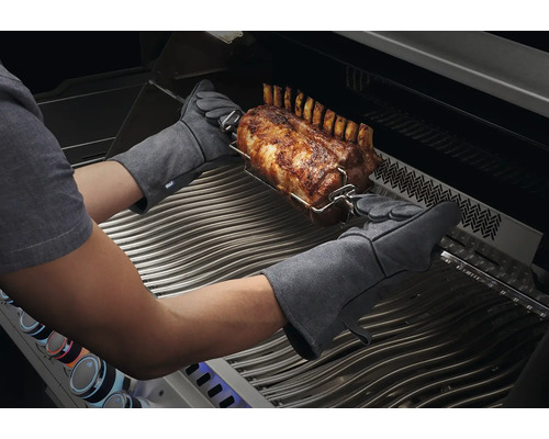 Person med grillhandskar hanterar en stek på ett grillspett i en grill.