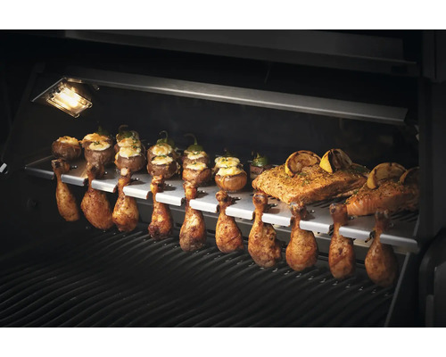 Olika rätter som kycklingklubbor, fyllda champinjoner och lax tillagas på en grill.