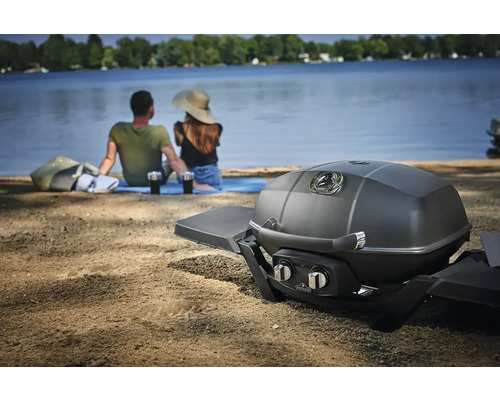 Bärbar grill vid sjön med ett par i bakgrunden.