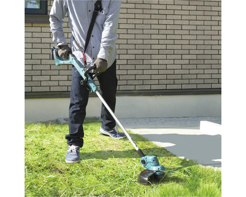 En person använder en batteridriven grästrimmer i trädgården för att trimma gräset.