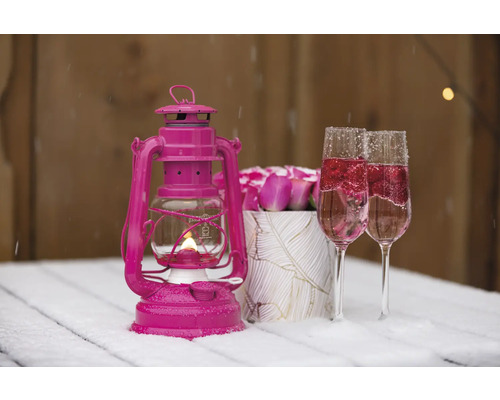 Dekorativ scen med rosa stormlykta, två fyllda glas och rosor på ett bord med snö