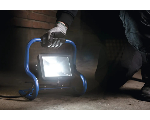 Person bär LED-byggstrålkastare med stativ