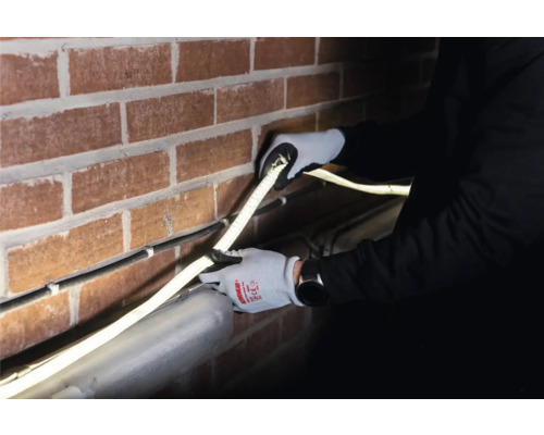 Installation av en LED-ljusramp på en tegelvägg av en person med skyddshandskar.