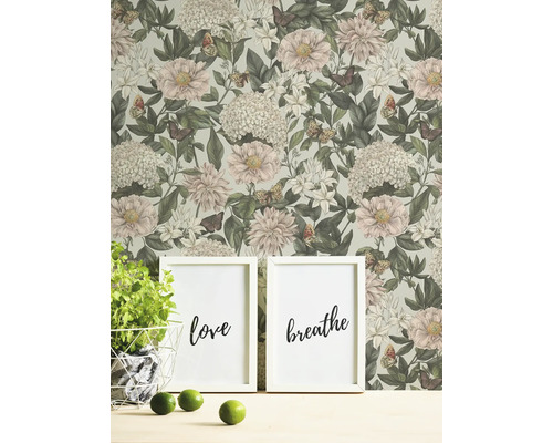 Vardagsrumsscen med blommig tapet, två inramade bilder med orden kärlek och andas, krukväxt och limefrukter