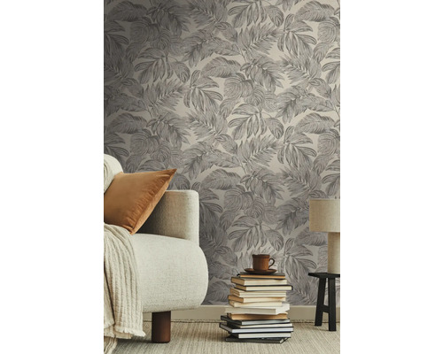 Vardagsrum med en tapet tryckt med löv, en soffa, en trave böcker och en lampa.