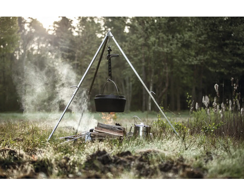 Gjutjärnskittel hänger över en lägereld på ett stativ utomhus.