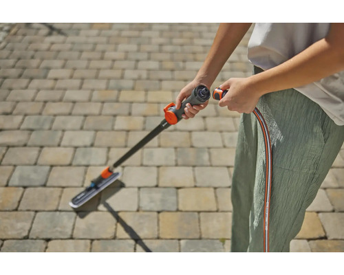 En person ansluter en altanrengörare till en trädgårdsslang för rengöring av utomhusutrymmen.