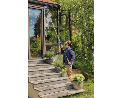 Man rengör fönster i en vinterträdgård med fönsterskrapa och teleskopskaft.