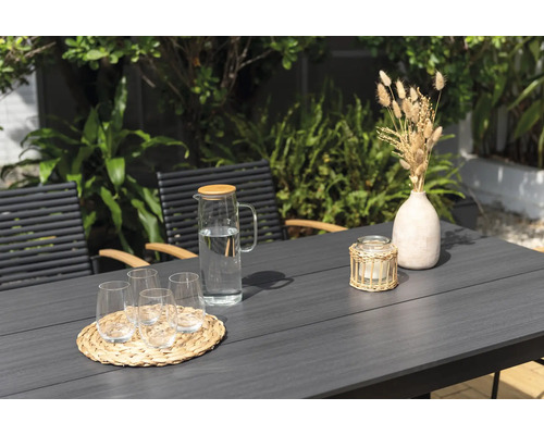 Trädgårdsscen med bord, stolar, glas, vattenkaraff, ljus och dekoration.