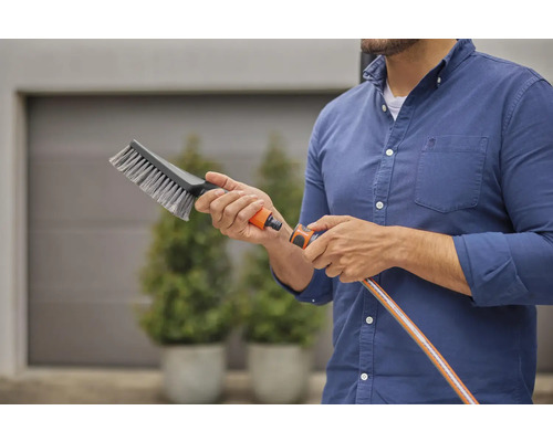 En person håller en tvättborste med vattenanslutning och en trädgårdsslang i handen.