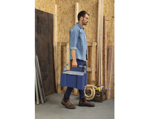 Man bär en blå verktygslåda genom en verkstad