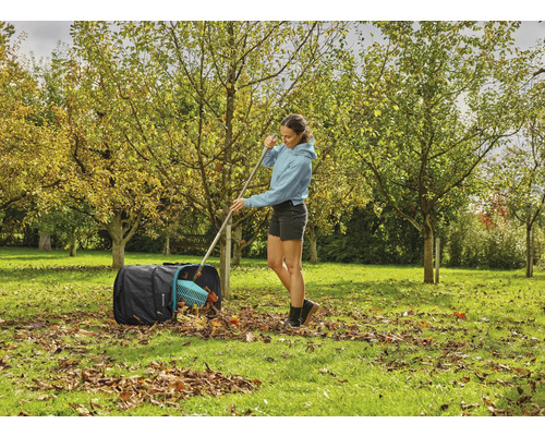 Kvinna krattar höstlöv i en lövsäck i trädgården