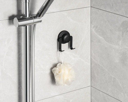 Svart sugkoppskrok med duschsvamp på kakelvägg bredvid duschstång