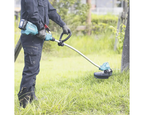 En person använder en Makita batteridriven grästrimmer i trädgården.