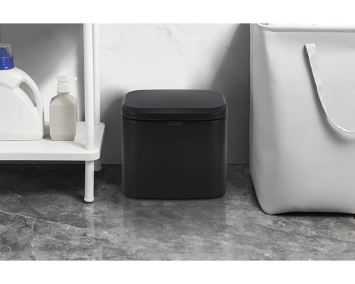 Svart pedalhink i badrummet bredvid en hylla och en tvättkorg.