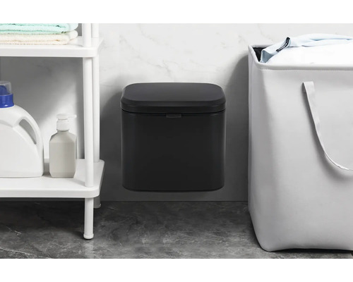 Väggmonterad papperskorg bredvid en tvättkorg och en hylla