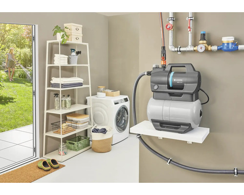 Hydroforpump i en tvättstuga med hylla och tvättmaskin, medan en kvinna vattnar i trädgården
