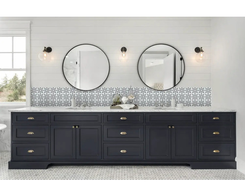 Badrum med blått tvättställsskåp, två runda speglar och mönstrade kakelplattor