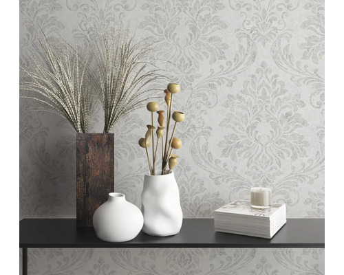 Dekorativt stilleben med vaser, prydnadsväxter, ljus och bok på en konsol framför en mönstrad tapet