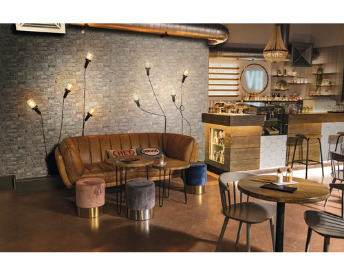 Interiör av ett kafé med soffa, bord, pallar och vägglampor framför en tegelvägg