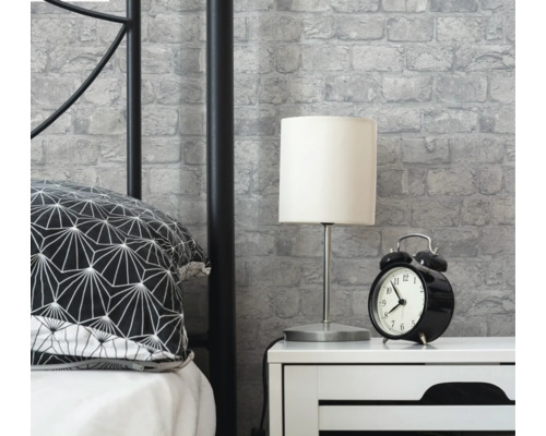 Sovrumsscen med säng, sängbord, lampa, väckarklocka och murverkstapet