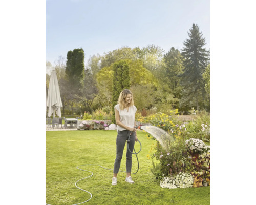 Kvinna vattnar blommor med en trädgårdsslang i trädgården.