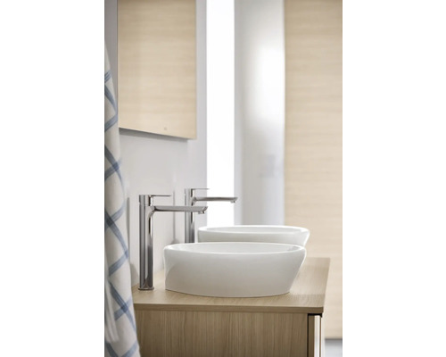 Badrum med två keramiska handfat och kranar på ett underskåp i trä