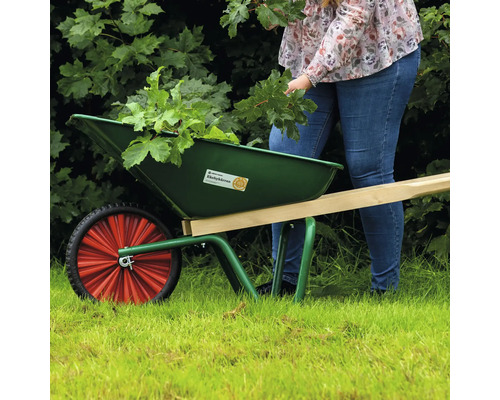 En grön skottkärra med ett hjul och trähandtag i trädgården, fylld med gröna växter.