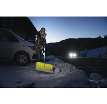 Kvinna skottar snö med en snöskyffel framför en bil.