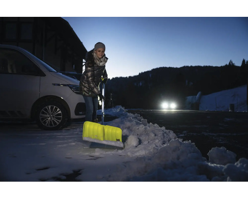 Kvinna skottar snö med en snöskyffel framför en bil.