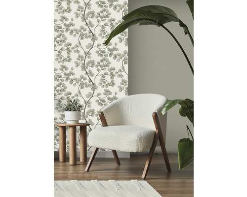 Miljöbild med blommig tapet, fåtölj, sidobord, matta och krukväxt.