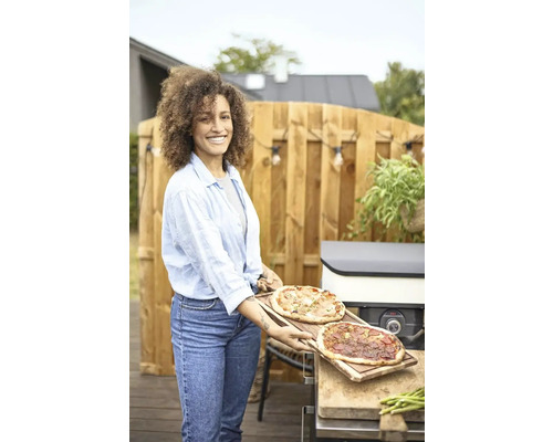 Kvinna med två pizzor på träbrädor i trädgården vid pizzaugnen