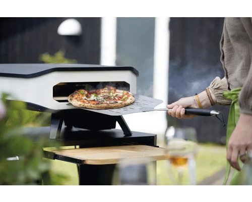 Pizzaugn med pizza på pizzaspade framför ugnen