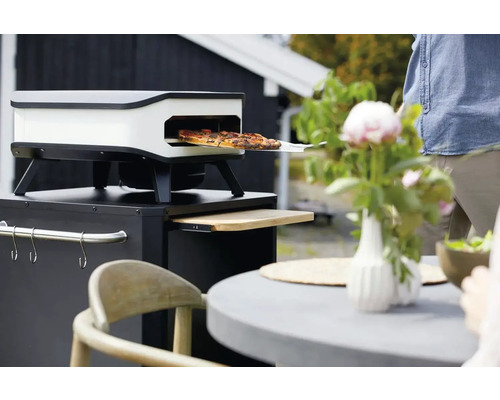 Pizza ugn på ett trädgårdsbord med pizza på en pizzaspade