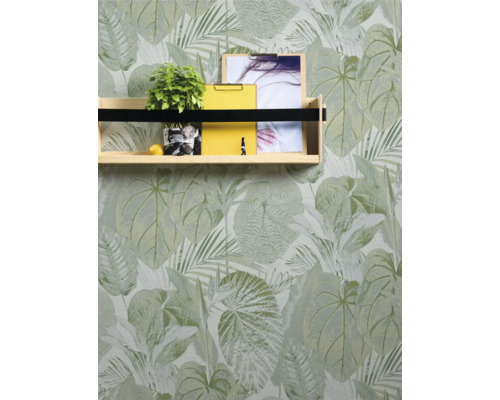 Hylla med växt, anteckningsblock och foto framför en tapet med bladmönster